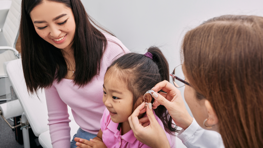 Consultation avec un professionnel audioprothésiste équipant un enfant  d'un appareil auditif avec l'accompagnement de sa mère. 